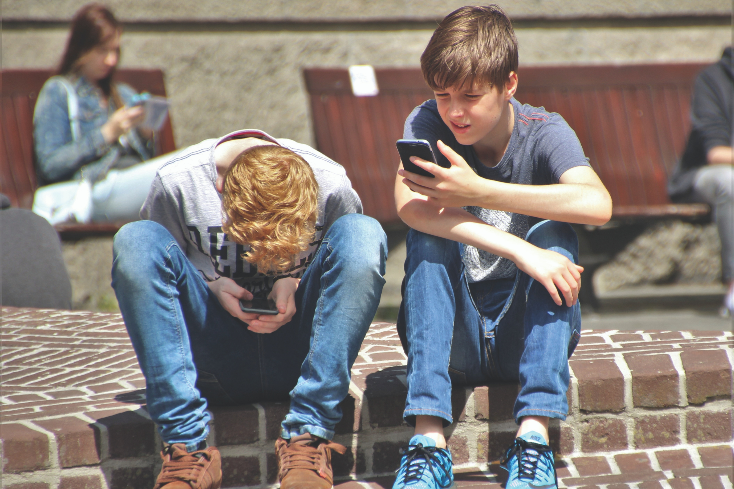 two preteen boys sit on a step looking at their smartphones